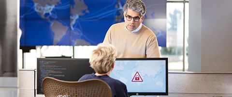 Two people facing each other with a computer monitor in between them displaying a threat warning