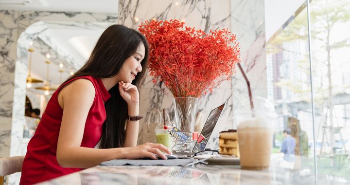 Mujer sentada junto a la ventana de una cafetería trabajando con su computadora
