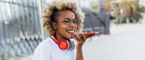 A person walking outdoors smiles while talking on a mobile phone.