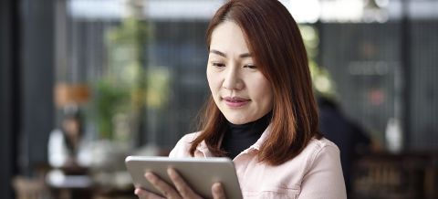 Woman in a pink shirt looking down at a tablet device in her hands