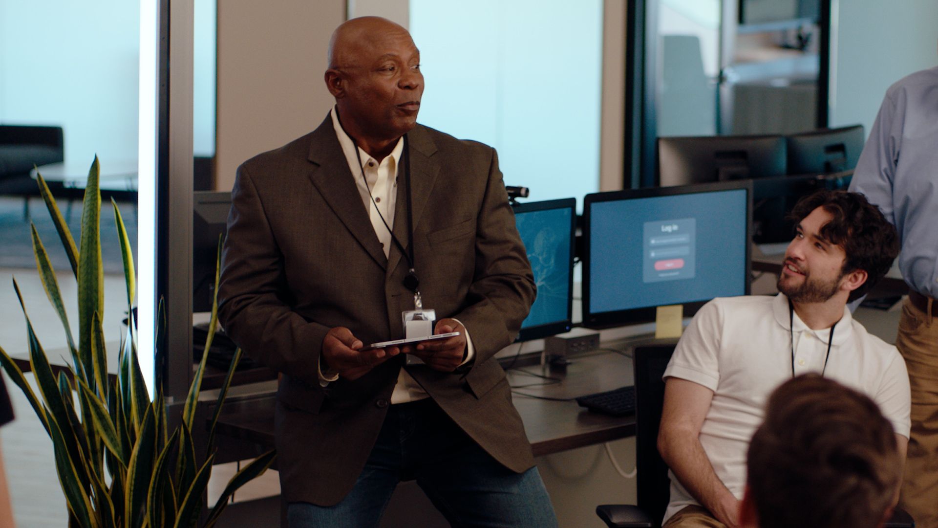 Business professional stands and speaks to people in open office while coworkers listen. 