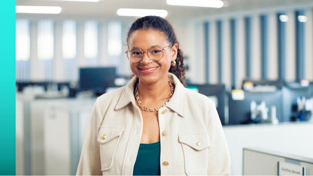 Person in business attire standing in an office setting smiling.