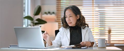 Business professional sits at a desk and works from a laptop.