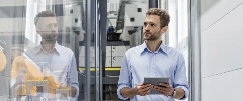 IT professional in a data center holding a tablet looking at equipment behind glass 