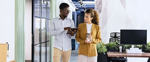 Two business colleagues discussing and reviewing content on computer tablet walking in hallway. 