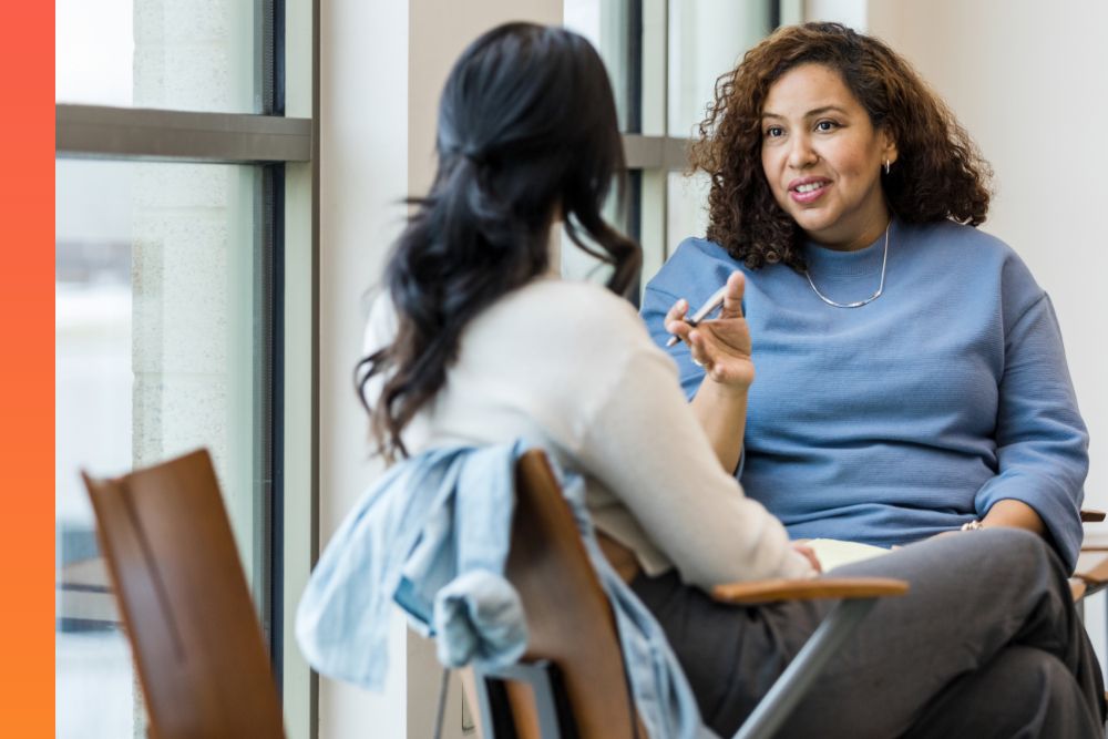 Woman in a blue sweater sitting and talking to a person sitting across from her