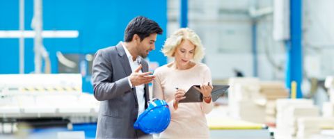 Man and woman standing on a factory floor while looking at a tablet device