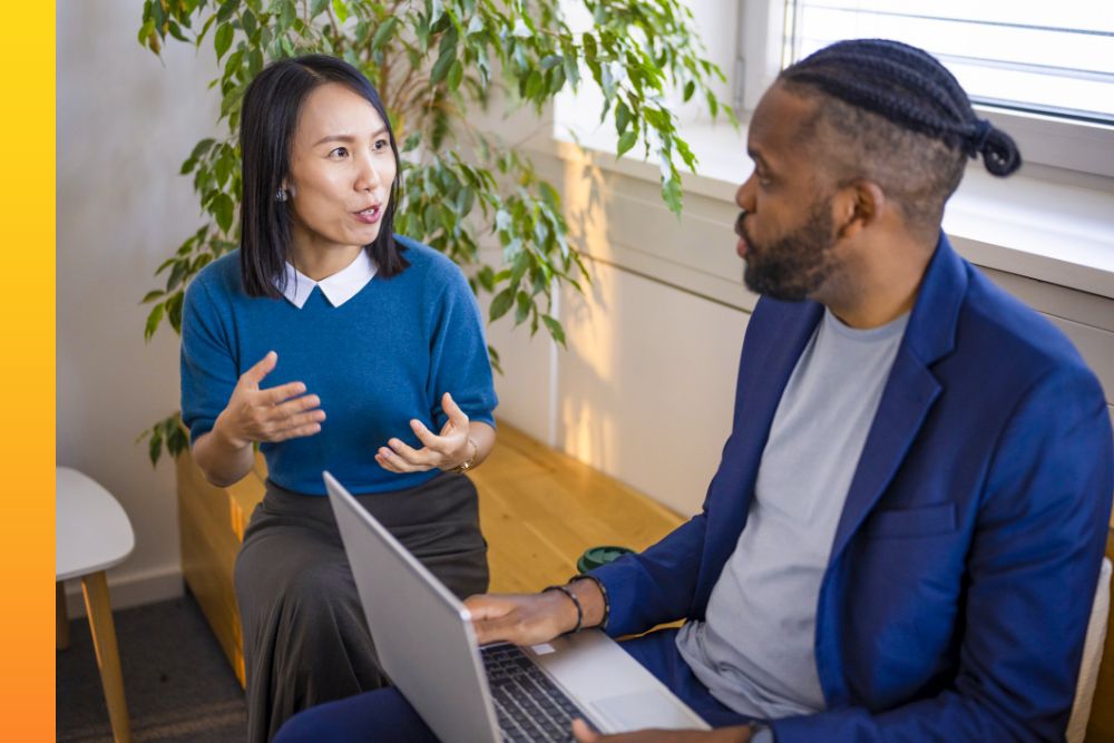 Two businesspeople sit and discuss something with a laptop open