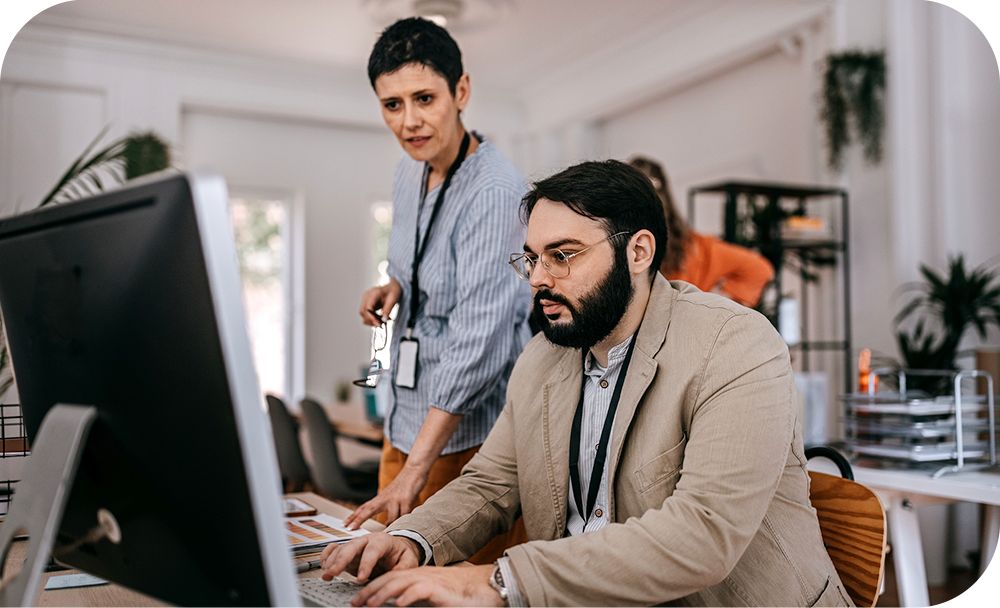 Two businesspeople look at a desktop monitor and converse