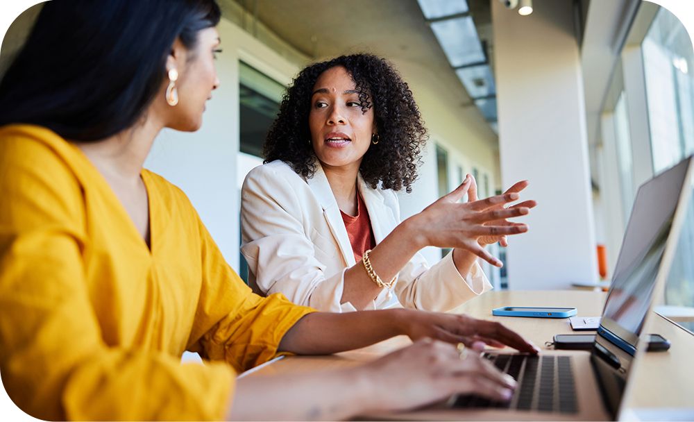 wo businesspeople converse while referencing an open laptop in front of them