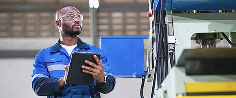 A person using a tablet device while looking at a piece of machinery