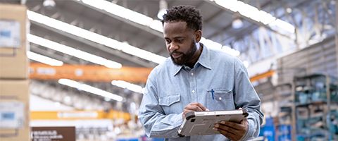 A person in a factory or warehouse holds a tablet and looks down at something off camera