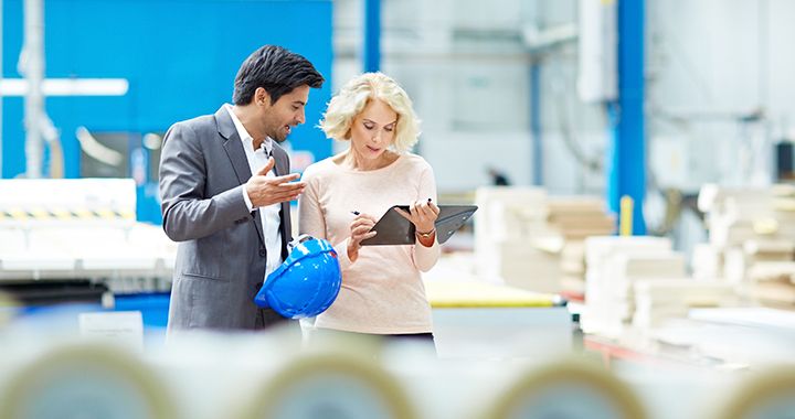 Two business people walking through a factory while working on a tablet device