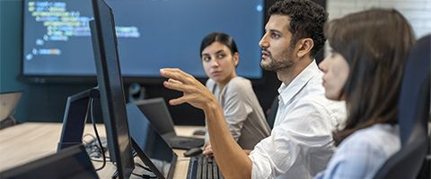 Three coworkers look at a computer screen while engaged in conversation 