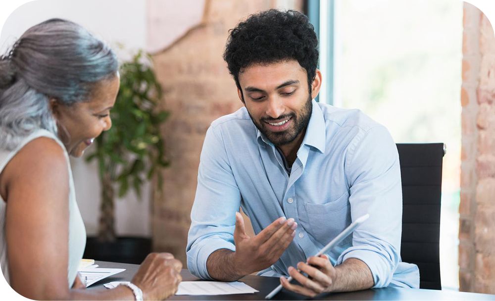 Two people in casual business attire smile and talk while looking at a tablet in an office