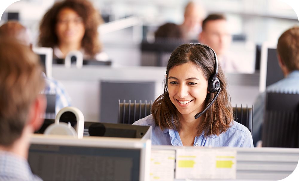 A call center representative smiles and talks on a headset in a busy office