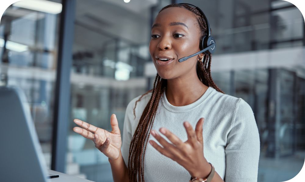 Woman sitting at a desk while talking on a head set and gesturing to her computer monitor