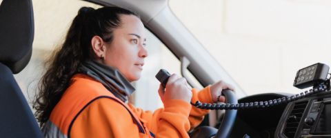 Woman in an orange jacket talking through a radio system while driving