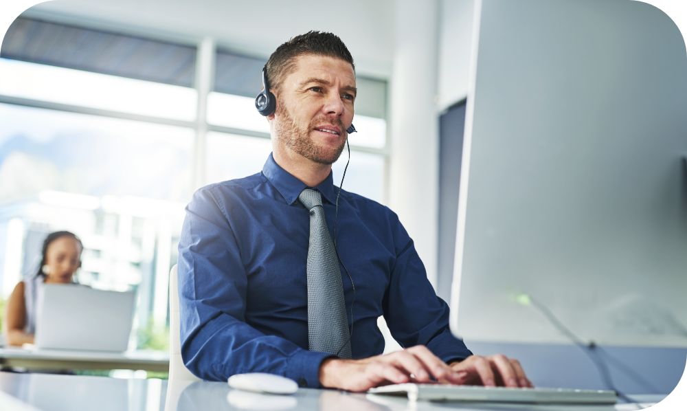 Man in a head set sitting at a desk while working on a desktop computer