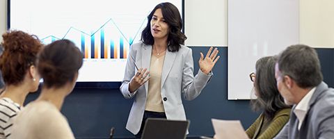 A person in a suit jacket gives a presentation in front of a board with a graph.