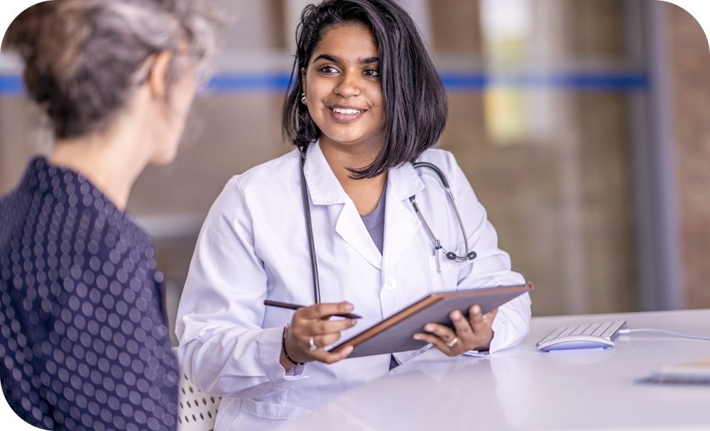 Physician sitting at a table with a notepad smiling at another person.