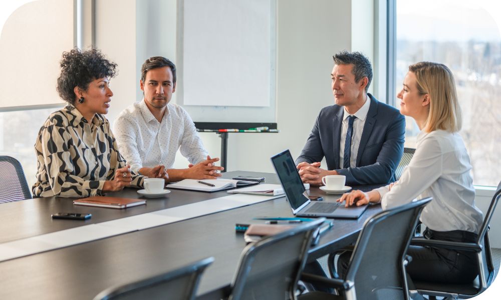 Four people in business attire sitting at a conference table having a discussion.