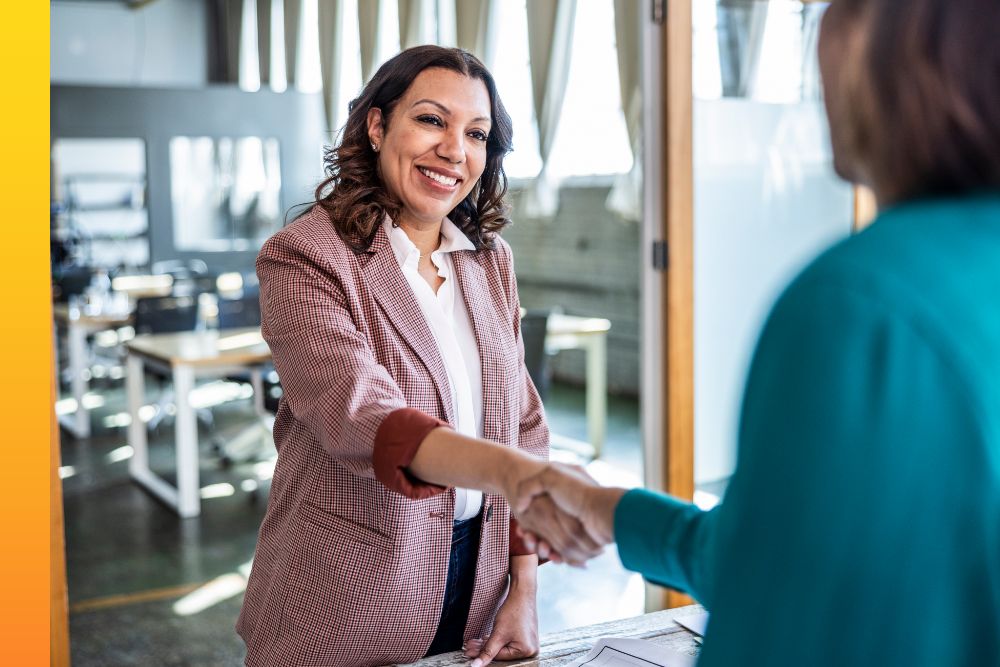 Business woman shaking hands with another person while standing above a table of prints