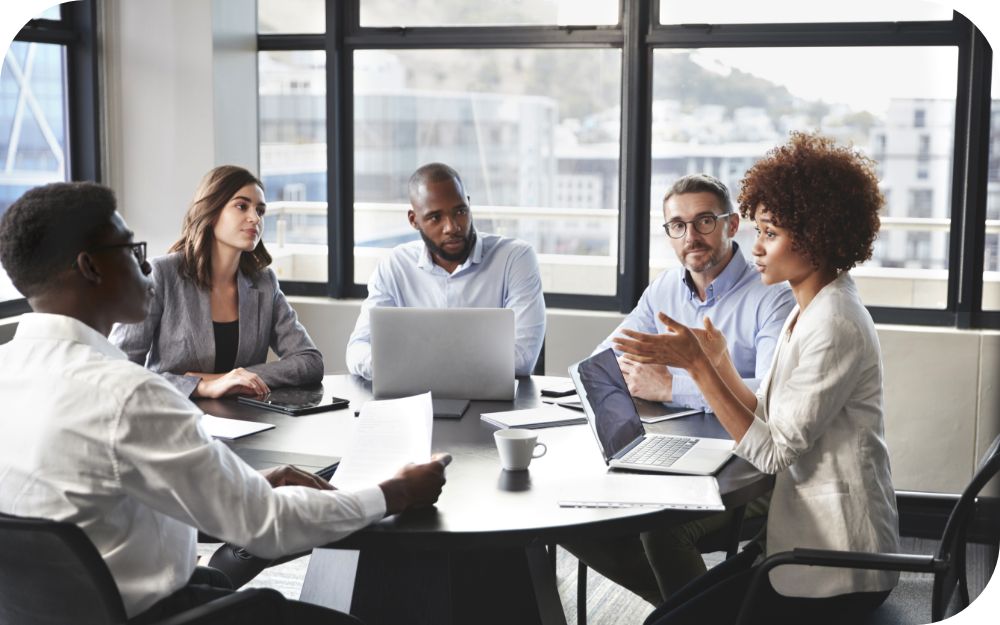 Five people engaged in a meeting or discussion seated around a table in a modern office setting.