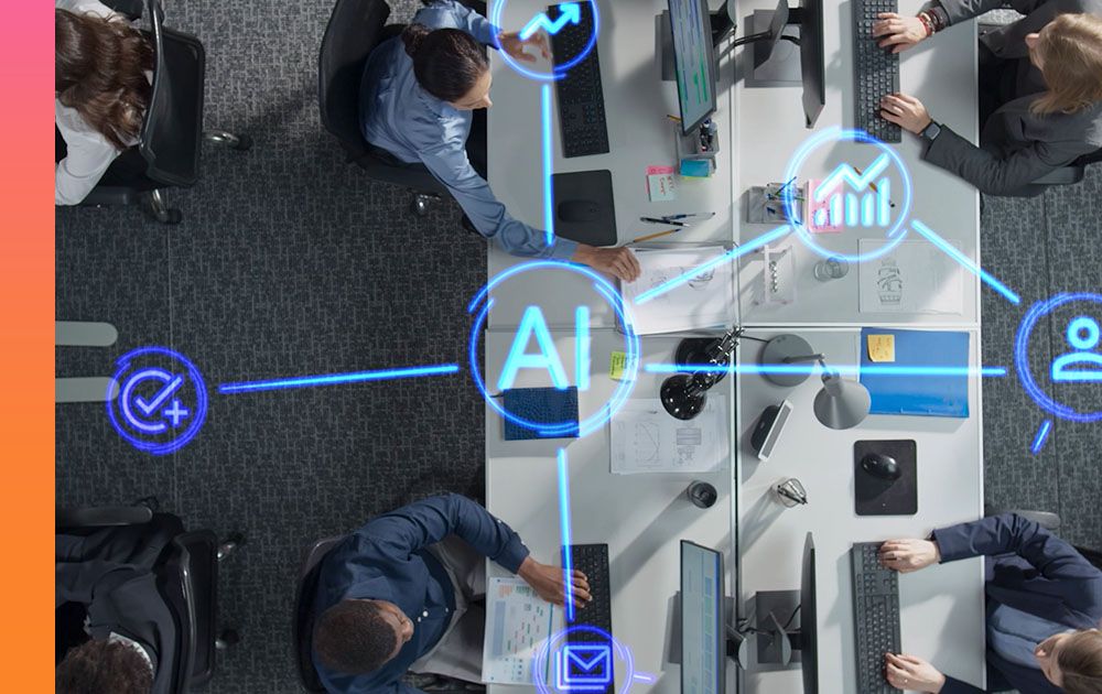 Overhead view of people sitting at tables in an office using keyboards and monitors overlaid with a circle in the center containing the letters AI connected by lines to icons representing digital processes