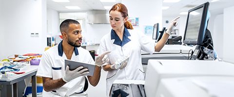 Two pharmacy workers collaborating as one holds a tablet and the other points at a computer screen