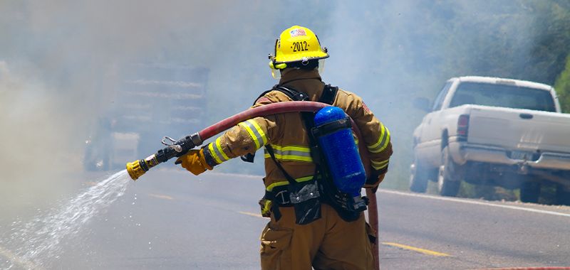 Fireman holding water hose walking through smoke