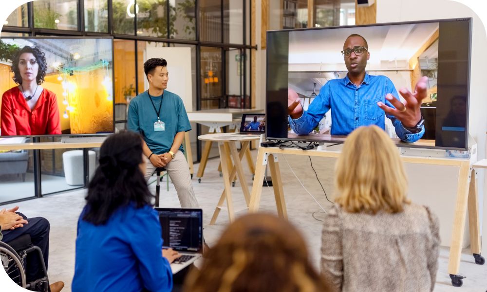 People sitting in front of two screens where two other people are joining a meeting via video call