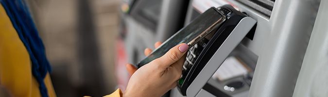 Nahaufnahme einer Hand, die ein mobiles Gerät an ein Kartenlesegerät hält, um eine Zahlung vorzunehmen