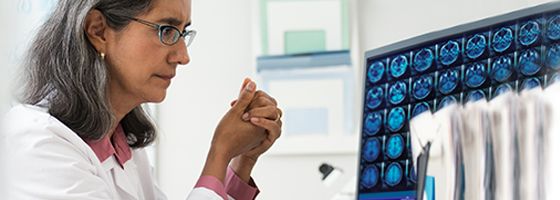 Frau in einem Laborkittel, die sich auf einem Computermonitor auf ihrem Schreibtisch Gehirnscans ansieht