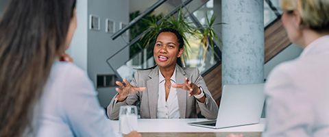 A woman converses with a man at a work desk.