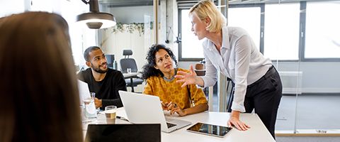 Woman leaning on conference table discussing important issues with colleagues with open laptops. 