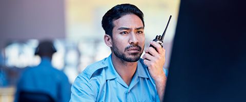 Man with cell phone walkie talking reviewing critical data on computer monitor in 911 call center. 