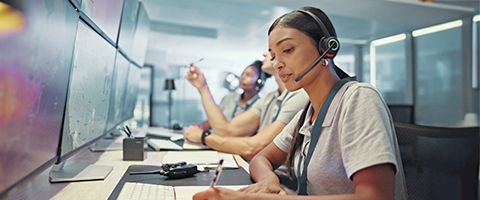 Employees make calls while sitting at desks with computer monitors, wearing headsets and taking notes 
