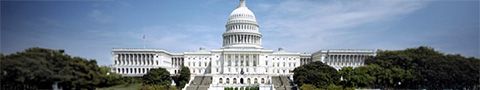 Wide exterior view of the U.S. Capitol building in Washington, D.C., with its white dome centered against a blue sky and surrounded by trees