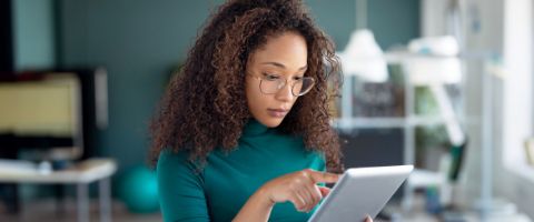 Person with glasses holding a smart tablet and touching the screen.