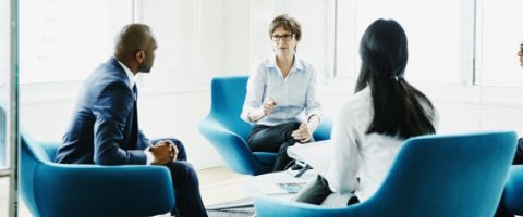 Three people sitting in a circle on blue chairs while talking amongst themselves