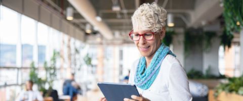 A person smiles at a tablet they’re holding in a bright office with plants.