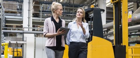 Two people walk through a warehouse and talk while one is holding a tablet device