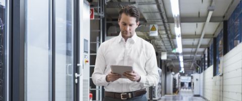 A person in business attire looks at a tablet device while standing in a hallway