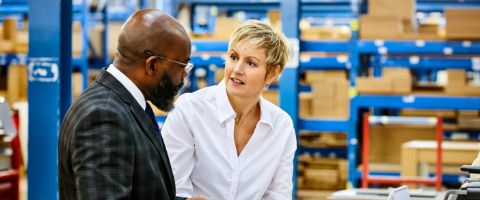 Two people have a conversation in a warehouse.