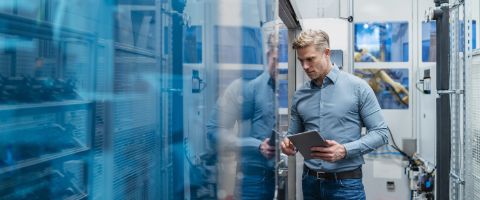 A person looking at a tablet stands next to a row of servers in a data center