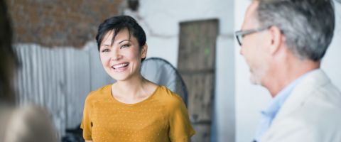 A person in a yellow blouse smiles and talks to someone.