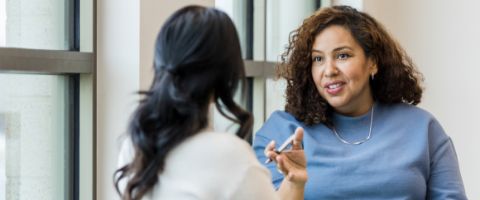 A person holding a pen talks to another person 