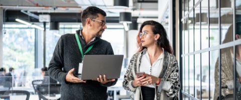 Man in glasses holding a laptop while talking to a woman in glasses holding a phone next to him