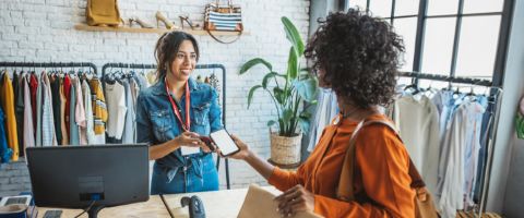 A retail worker and a customer smiling and completing a transaction with a smartphone.